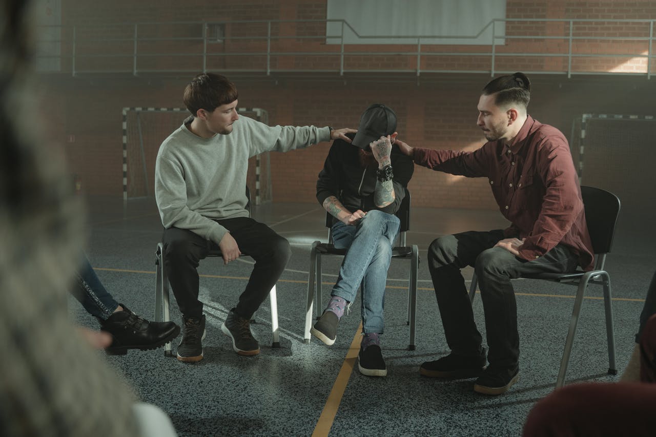 Three men in a gymnasium engaged in a supportive group therapy session.