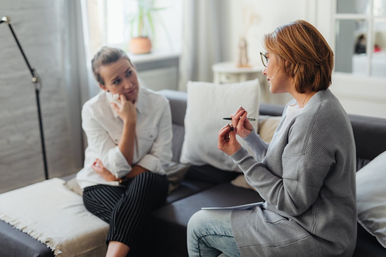 about-01 Two women, one being a therapist, engaging in a thoughtful conversation on a couch in a cozy room.