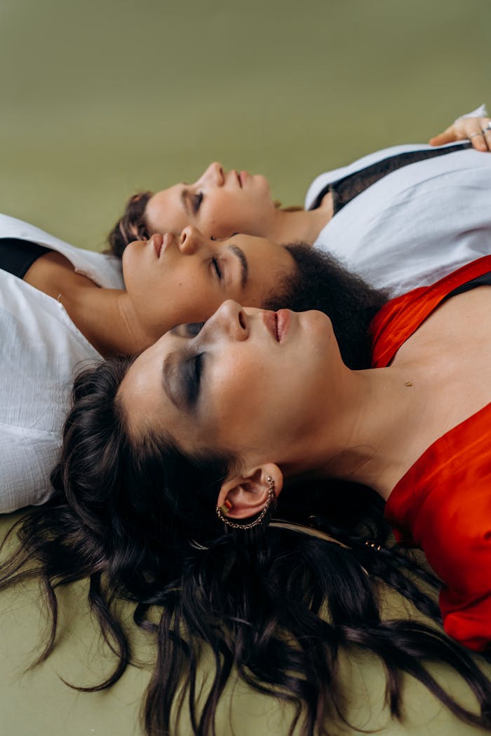Three women lying down with closed eyes, embracing relaxation and spirituality.